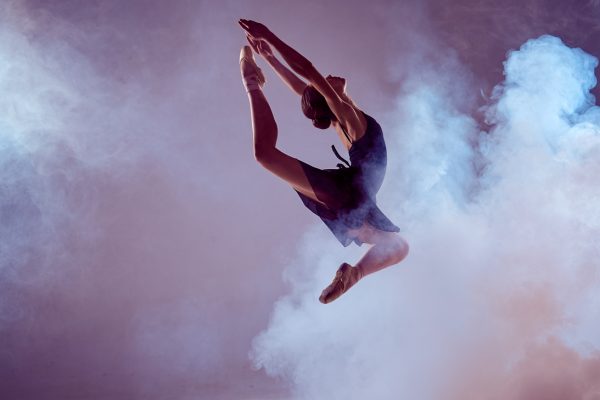 young ballet dancer jumping on a lilac background. Ballerina is wearing in blue dress and pointe shoes. The outline shooting - silhouette of girl with smoke effect